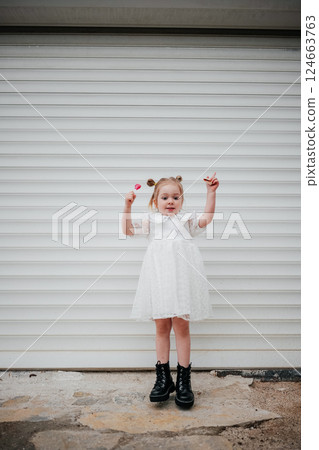 Young girl in a white dress posing with hands raised and wearing large black boots Young girl in a white dress posing with hands raised and wearing large black boots 124663763