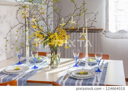 Elegant Easter and spring table setting with a handmade of wire eggs decoration and a bouquet of mimosa in a glass vase. 124664018