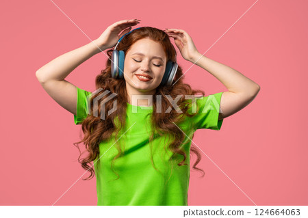 Happy woman gets high, listening music, enjoying sound with headphones on pink Happy woman gets high, listening music, enjoying sound with headphones on pink 124664063