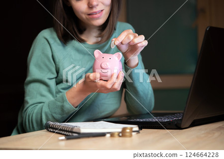 The girl puts her savings in a piggy bank. The girl puts her savings in a piggy bank. 124664228
