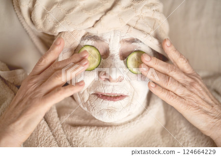 Old woman applies a white mask on her face. Old woman applies a white mask on her face. 124664229