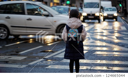 Young girl waiting at a crosswalk in urban traffic 124665044