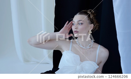 Sophisticated woman posing gracefully against monochrome backdrop, highlighting elegant jewelry and makeup with contemplative sideways gaze 124666206