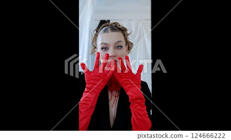 Elegant woman wearing vivid red gloves and sleek black dress, striking dramatic pose against minimalist backdrop, highlighting haute couture styling with confident demeanor 124666222