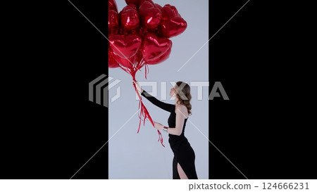 Elegant female model holding red heart shaped balloons, embodying romantic celebration with graceful pose and joyful expression against soft background Elegant female model holding red heart shaped balloons, embodying romantic celebration with graceful pose and joyful expression against soft background 124666231