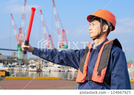 A man in work clothes directing traffic at a port 124667925