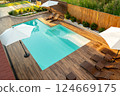 Stylish backyard with turquoise swimming pool, wooden deck, lounge chairs, and white umbrellas 124669175