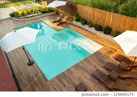 Stylish backyard with turquoise swimming pool, wooden deck, lounge chairs, and white umbrellas Stylish backyard with turquoise swimming pool, wooden deck, lounge chairs, and white umbrellas 124669175