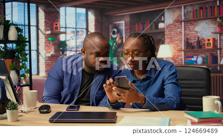 African american man and woman solving freelance tasks at home, working together on their phones to finish an important project for their employer. Networking with partners. Camera A. African american man and woman solving freelance tasks at home, working together on their phones to finish an important project for their employer. Networking with partners. Camera A. 124669489