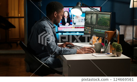 Young filmmaker working on media post production from agency office, ensuring editing timeline and color grading for a video shoot. Tech driven workspace showcases a digital workflow. Camera B. Young filmmaker working on media post production from agency office, ensuring editing timeline and color grading for a video shoot. Tech driven workspace showcases a digital workflow. Camera B. 124669561