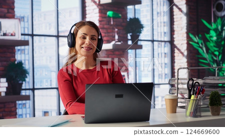 Tech savvy user working on a laptop and listening to focus music at home, enjoying freelancing tasks and multitasking. Cheerful woman having fun with great rhythm, productive lifestyle. Camera A. 124669600
