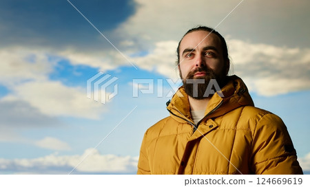 Adventure seeker in warm clothing enjoys the serenity of the wilderness, panoramic mountain top view and open sky create the perfect setting for relaxation. Cold winds uphill. Camera B. Adventure seeker in warm clothing enjoys the serenity of the wilderness, panoramic mountain top view and open sky create the perfect setting for relaxation. Cold winds uphill. Camera B. 124669619
