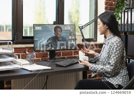 Businesswoman seated at office desk, using computer for video call with african american colleague, discussing business strategies. Asian female manager and client connecting remotely. Businesswoman seated at office desk, using computer for video call with african american colleague, discussing business strategies. Asian female manager and client connecting remotely. 124669659