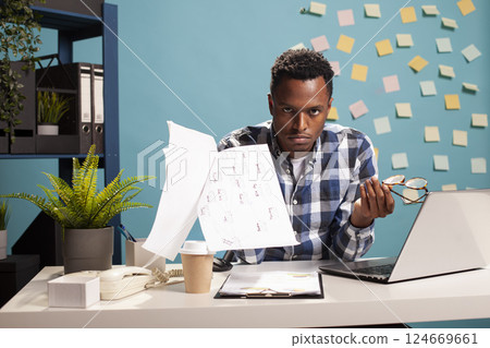 Businessman seated at desk, tossing papers in air due to work stress, facing challenges like debt and potential bankruptcy. Angry project manager holding documents and glasses, angrily looks at camera Businessman seated at desk, tossing papers in air due to work stress, facing challenges like debt and potential bankruptcy. Angry project manager holding documents and glasses, angrily looks at camera 124669661