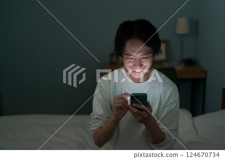 A man operating a smartphone in a dark room 124670734