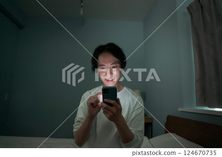 A man operating a smartphone in a dark room A man operating a smartphone in a dark room 124670735