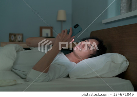 一名男子在床上使用智慧型手機 124671049
