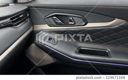 Door handle with power window control buttons. Black perforated leather interior with stitching. Modern car black leather interior details. Door handle with power window control buttons. Black perforated leather interior with stitching. Modern car black leather interior details. 124671389