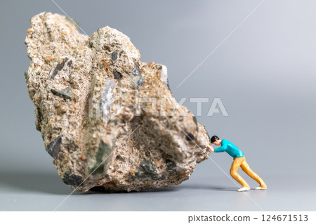 A tiny figurine of a man pushing a massive rock, symbolizing perseverance, struggle, and determination. A tiny figurine of a man pushing a massive rock, symbolizing perseverance, struggle, and determination. 124671513