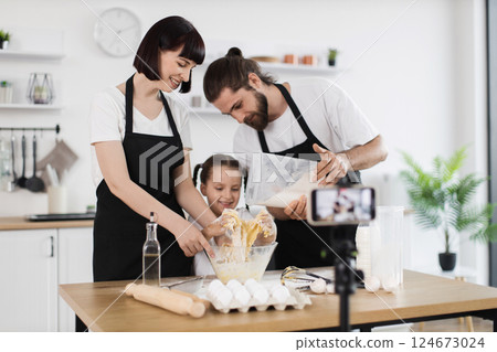 Caucasian man, woman, and child baking in kitchen wearing black aprons recording cooking process. 124673024