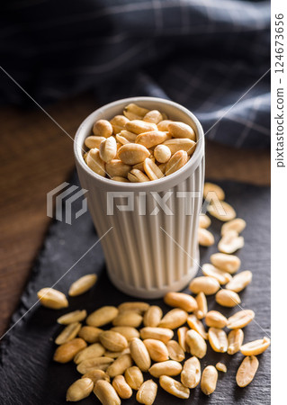 Roasted salted peanuts in cup on wooden table. 124673656