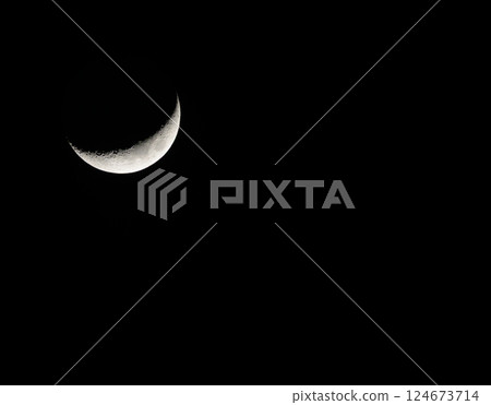 The sharp crescent moon shining in the night sky contrasts with the deep darkness 124673714
