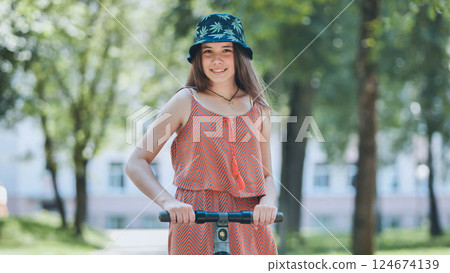 Teenage rider gripping electric scooter handlebar, riding through lush green park under bright sunlight 124674139