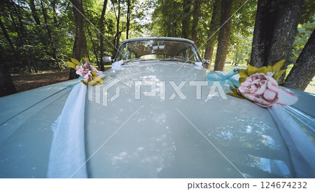White vintage car decorated with flower bouquets and ribbons, parked in a forest, ready for a wedding ceremony 124674232