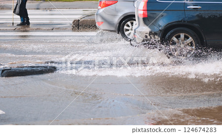 Vehicles navigating water covered urban roadway, spraying liquid during intense rainfall 124674283