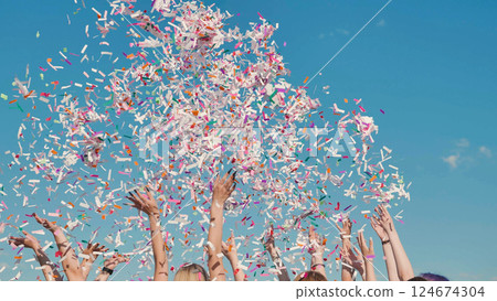 Students throwing confetti in the air during graduation ceremony celebrating their academic achievement under blue sky 124674304