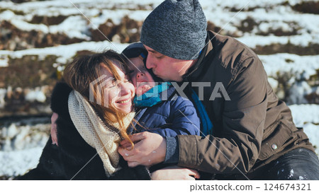 Family embracing, sharing warm moments while standing outdoors amid snowy winter scenery, displaying genuine love and connection 124674321
