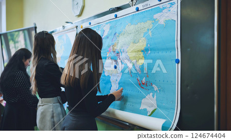 High school students are learning geography, positioning markers on a large world map hanging on the blackboard High school students are learning geography, positioning markers on a large world map hanging on the blackboard 124674404