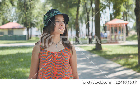 Teenage girl with bucket hat and cross necklace walking in a park during a sunny summer day 124674537
