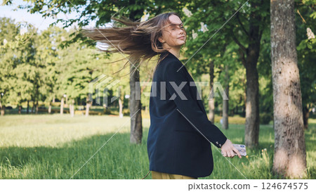Professional woman strolling through urban park, wind moving hair, smartphone in hand, experiencing midday work break moment Professional woman strolling through urban park, wind moving hair, smartphone in hand, experiencing midday work break moment 124674575