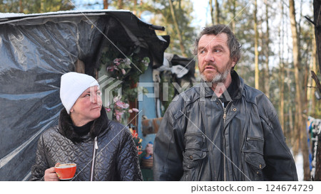Alcohol addicted homeless couple drinking coffee outside their makeshift home in a winter forest 124674729