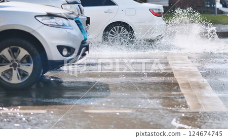 Splashing white vehicle sending water spray across urban roadway during bright daylight 124674745