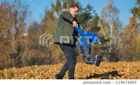 Father and son playing amid fallen autumn leaves, sharing joyful moment in sunlit park setting Father and son playing amid fallen autumn leaves, sharing joyful moment in sunlit park setting 124674805