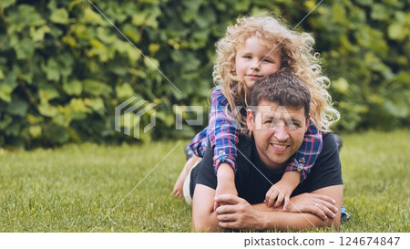 Father and daughter lying together on sunlit grass, sharing laughter and tender connection during outdoor family moment 124674847