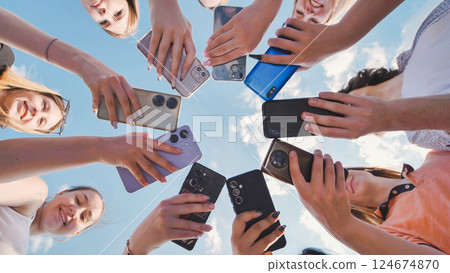 Students forming a circle with their smartphones against a blue sky background Students forming a circle with their smartphones against a blue sky background 124674870