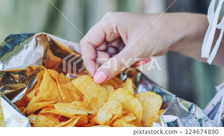Woman pulling crispy potato chip from foil bag, enjoying salty, crunchy snack with intense flavor sensation Woman pulling crispy potato chip from foil bag, enjoying salty, crunchy snack with intense flavor sensation 124674890