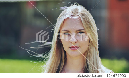 Blonde woman with light eyes and freckles posing confidently outdoors, her hair gently blowing in the wind 124674900