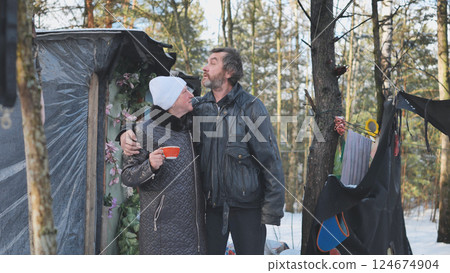 Desperate couple huddling together near ramshackle forest shelter, sharing intimate moment during harsh winter survival Desperate couple huddling together near ramshackle forest shelter, sharing intimate moment during harsh winter survival 124674904