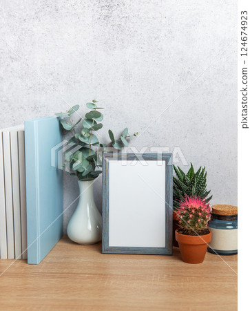 Blue picture frame standing on wooden desk with plants and books behind 124674923