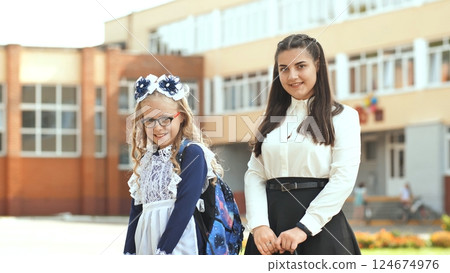Schoolgirl hugging mother, beaming beside school entrance during back to school moment 124674976