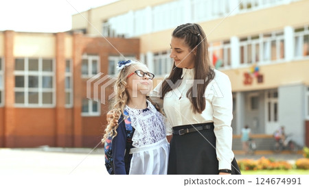 Two sisters hugging in front of their school in the first day of class, wearing school uniform 124674991
