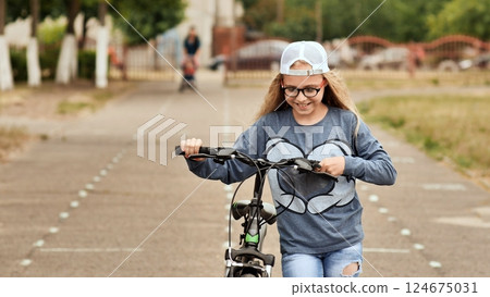 An eleven-year-old girl in a good mood rides a bicycle and after a stop shows a thumbs-up. 124675031