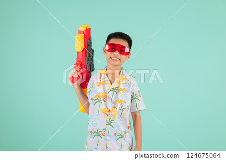 Songkran celebration as a joyful Thai child in glasses and a floral shirt holds a water gun 124675064