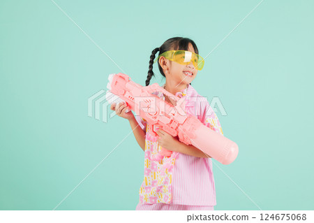 Songkran excitement as a joyful girl in glasses and a floral shirt holds a toy water gun Songkran excitement as a joyful girl in glasses and a floral shirt holds a toy water gun 124675068