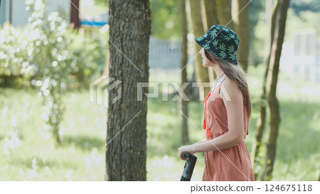 Woman wearing cannabis leaf bucket hat riding electric scooter during sunny park leisure moment Woman wearing cannabis leaf bucket hat riding electric scooter during sunny park leisure moment 124675118