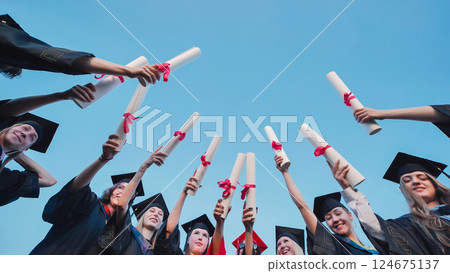 Happy students in graduation gowns proudly holding up their diplomas Happy students in graduation gowns proudly holding up their diplomas 124675137